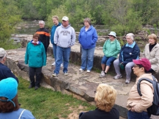 photo of a group of hikers sitting and standing at the Glencoe Dam listening to guest trail guide Bob Ellis sharing history of the Glencoe Mill