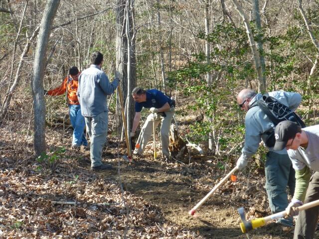 five men using tools to cut trail in the woods