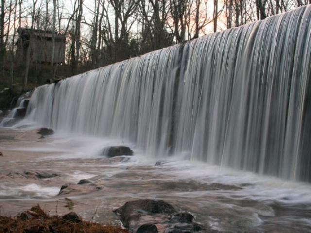 a photo of the river pouring over the dam at Altamahaw in the winter with an old farm structure in the background