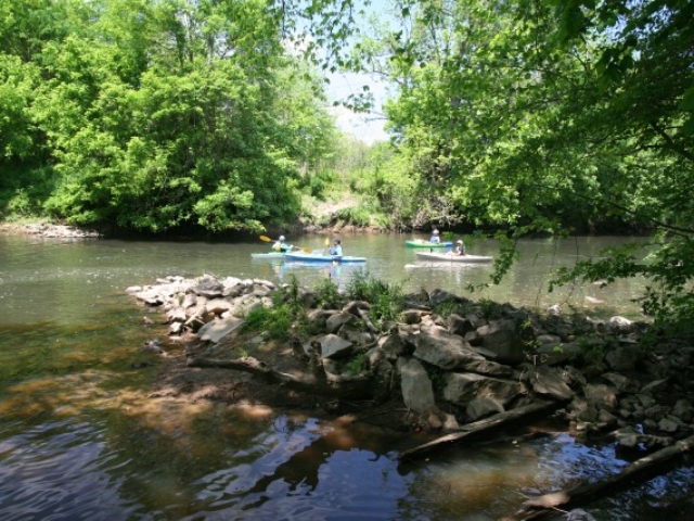 photo of four kayakers on the river at Indian Valley with a rocky island spit in the foreground and trees in the background