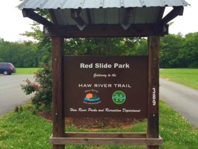 photo of the welcome sign at Red Slide Park with a tree and the parking area behind it