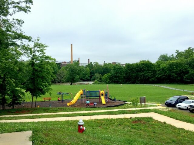 photo looking down on the playground at Red Slide Park with the field, river, and Granite Mill in the background and trees all around