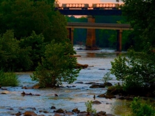 a view of the river from Red Slide Park at sunset with train cars on the traintrack bridge over the river