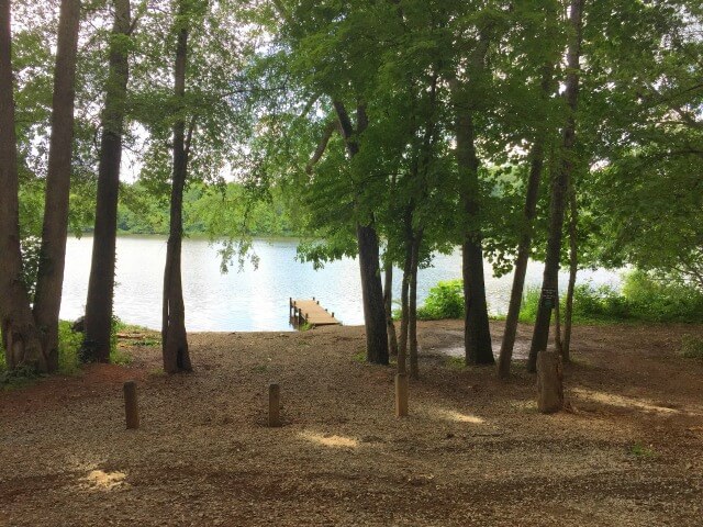 photo of the Saxapahaw Lake dock taken from the parking area looking out towards the river with trees in the foreground and trail entrance on the right