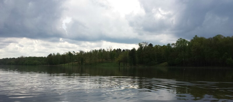 photo of rippling water on Saxapahaw lake with light and dark stormcloud sky and riverbank with trees in background