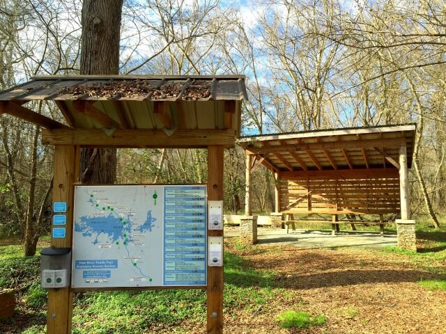 photo of welcome kiosk with river map in foreground and picnic shelter in background at Saxapahaw Mill Race Paddle Access