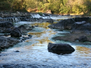 a photo of the dam remains at Swepsonville River Park during sunset with water flowing over the dam remnants