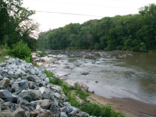 photo of the river with rocks in the river and a pile of rocks on the left foreground