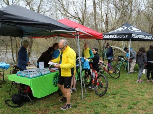 a registration table under two popup tents and a Performance Bicycle tent with staff working the registration table and participants with their bikes checking in