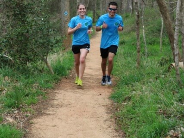 a male and female runner in blue event Tshirts running on the HRT during the Trailathlon with trees and grass on either side