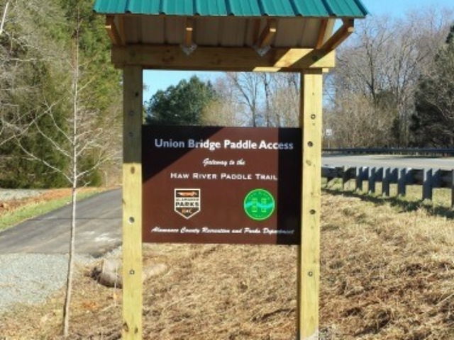 photo of the welcome kiosk at Union Bridge Paddle Access which has a brown sign and green roof set into a wood frame