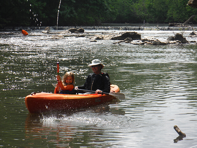 photo of dad and daughter in an orange kayak with dad holding the paddle and daughter playing with a watergun