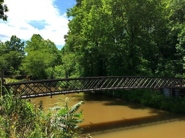 a photo of a metal pedestrian footbridge crossing the river at Altamahaw with trees in the background